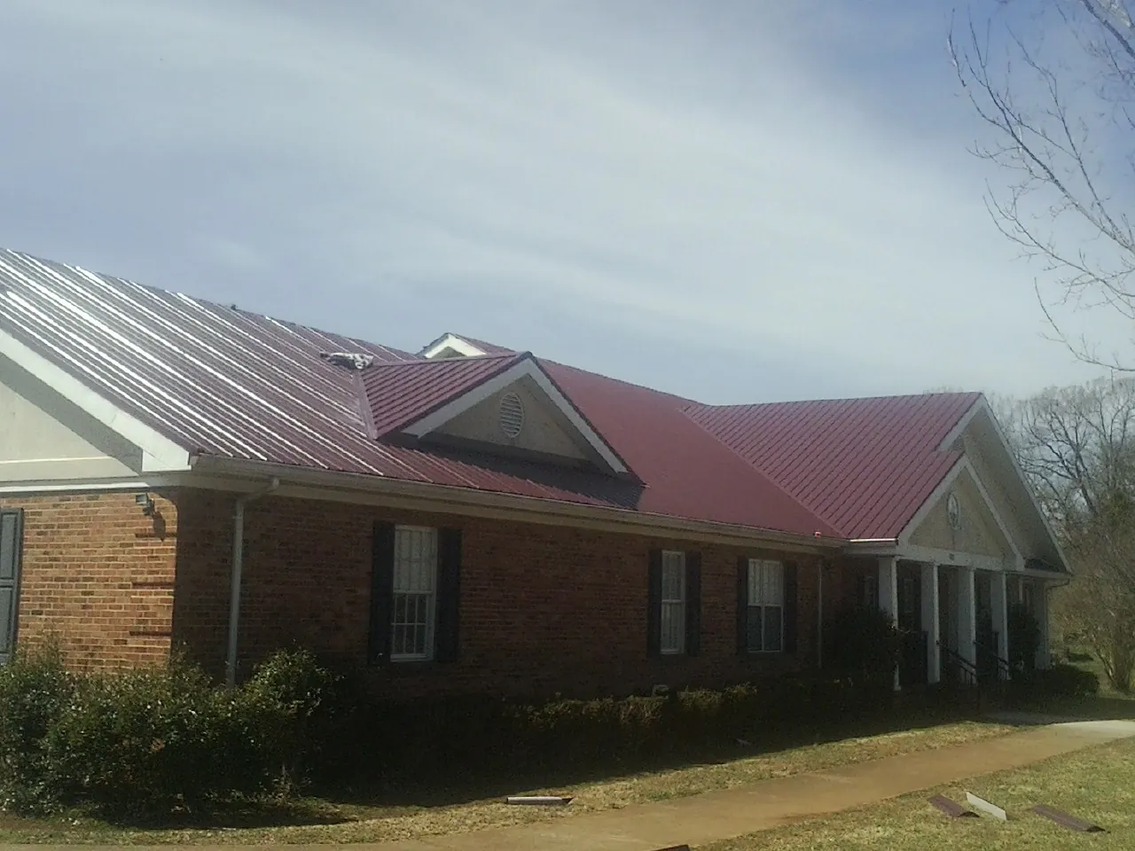 Red metal roof with gabled entries on a long brick building, from a Hail Damage Roof Repair job in Arco
