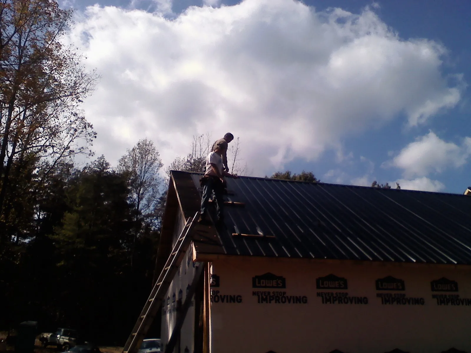 Roofer fastening dark metal panels high against a cloudy sky, from a Roof Inspection job in Arco