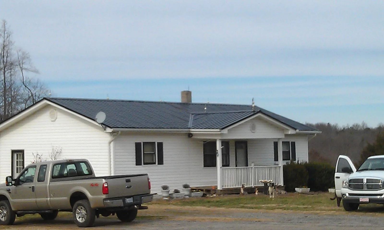 Finished dark metal roof on a white ranch home with work trucks parked in Arco